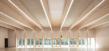 Im Innen der Kulturhalle dominieren helle Sichtholzflächen, der Blick schweift durch die fast gebäudebreite Glasfront in den direkt angrenzenden Bienwald. 