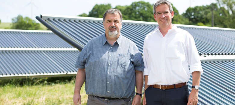 Ortsbürgermeister Volker Wichter und Michael Uhle, Klimaschutzmanager im Rhein-Hunsrück-Kreis, vor dem Solarthermie-Feld, welches das Nahwärmenetz von Neuerkirch-Külz unterstützt. 